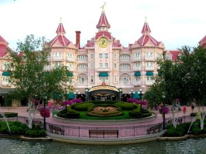 En esta imagen aparece un hermoso hotel en el gran parque de DisneyLand de París. Este es como un palacio rosa rodeado de jardines, uno de ellos tiene la cara del famoso personaje, Mickey Mouse.